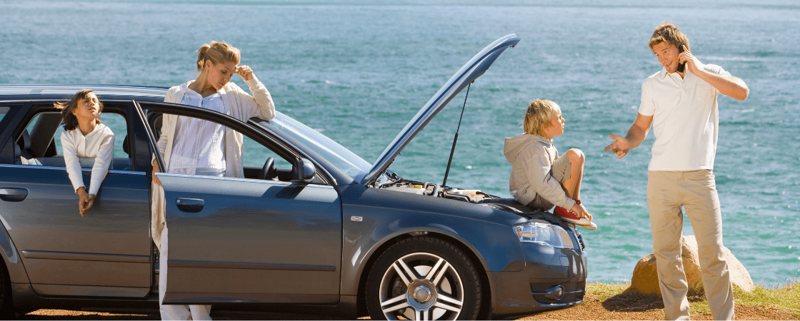 Eine Familie steht neben einem liegengebliebenen Auto am Straßenrand und wartet auf Hilfe
